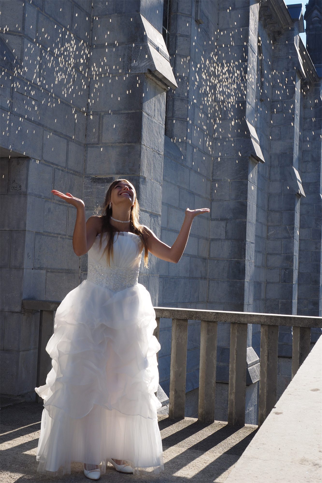 Éva Ostrowska throwing rice over herself against the blue stone of the basilica, Lourdes, 2016