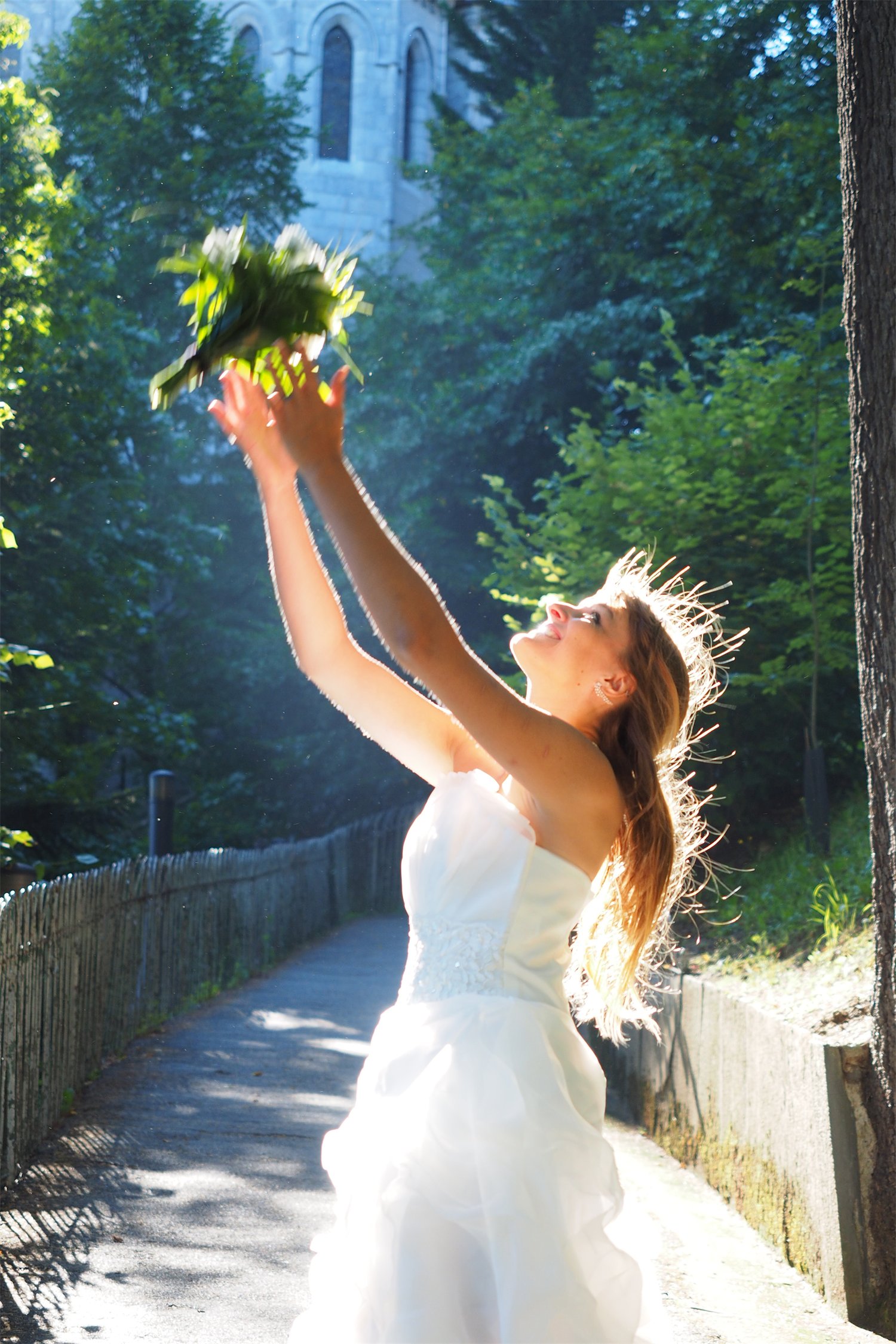&Eacute;va Ostrowska throwing her bouquet into the air and catching it herself on the path below the basilica of Lourdes, backlit, 2016